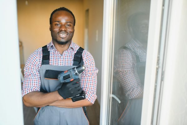 Close-up Of Young African Handyman In Uniform Installing Window